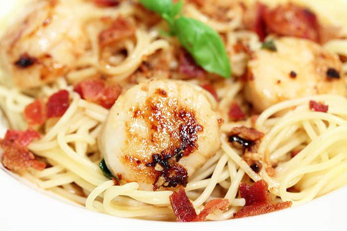 Closeup of pasta with scallops and bacon in white bowl.
