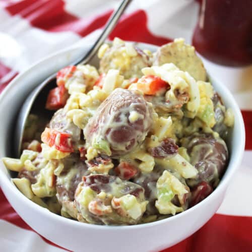 Red Potato Salad in white bowl with spoon on red striped table.