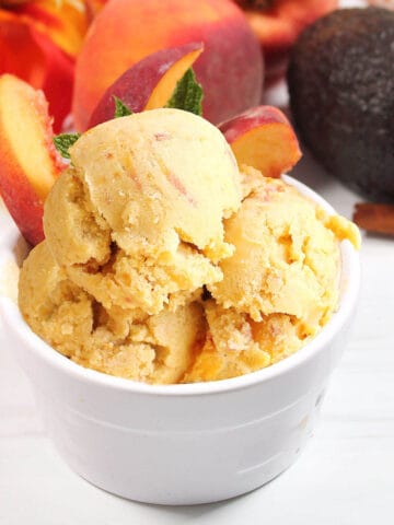 Healthy peach ice cream in dish with sliced peaches.