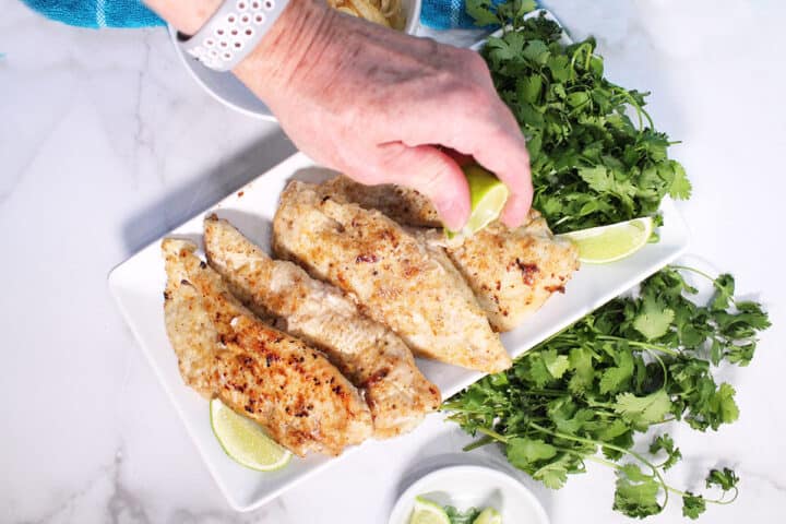 Squeezing lime over cooked chicken on white platter.