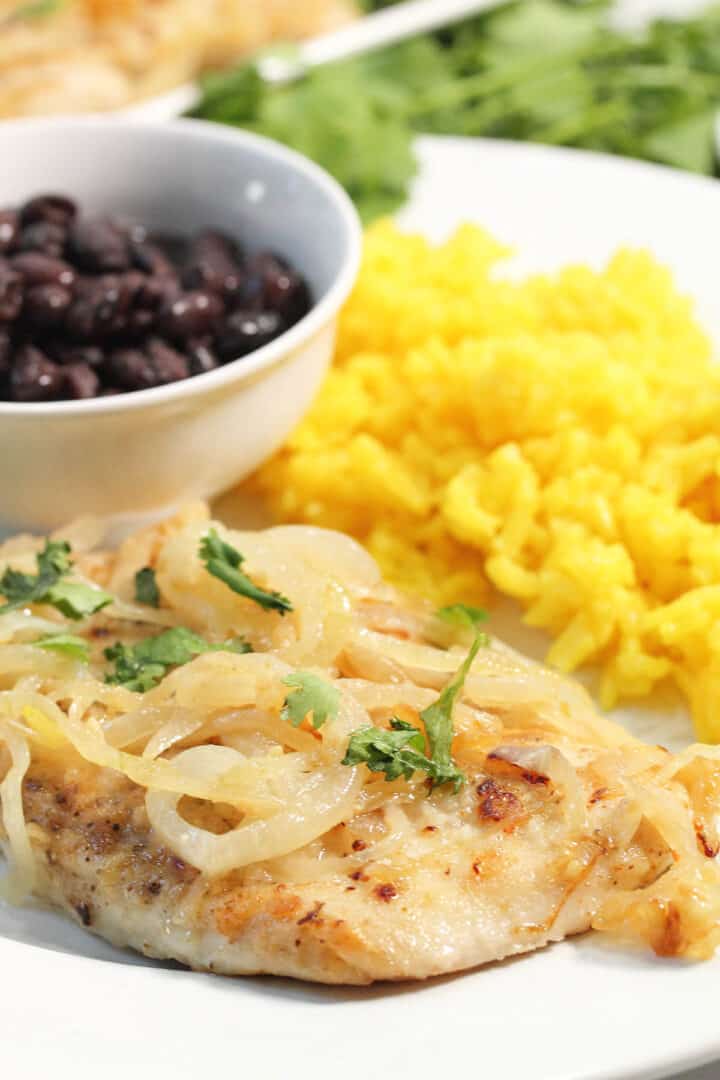 Closeup of chicken on dinner plate with rice and beans.