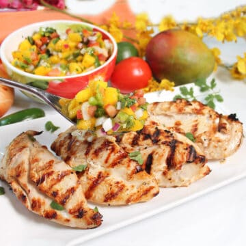 Holding spoonful of salsa with mango over grilled chicken.