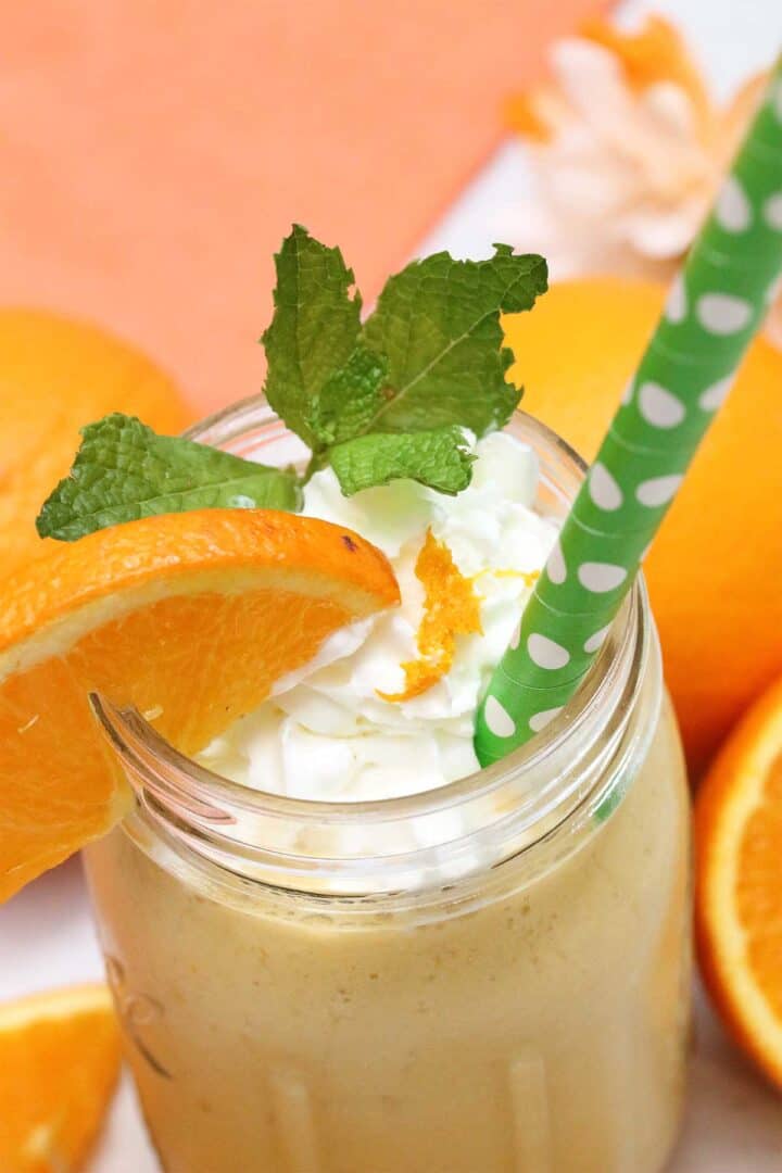 Looking down into smoothie with green polka dot straw, whipped cream and orange wedge.