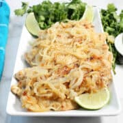 Chicken topped with onions on white platter with lime slices.