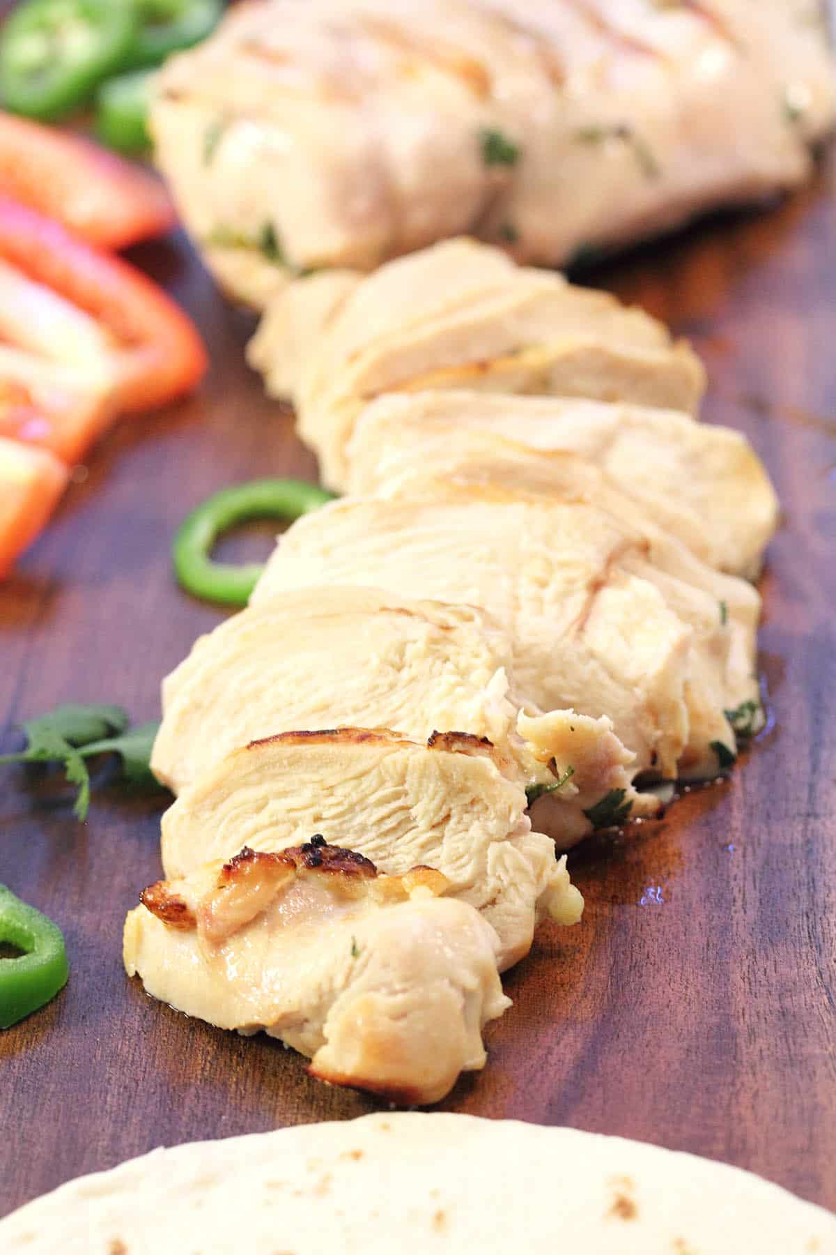 Closeup of moist sliced tequila lime chicken on wooden board.