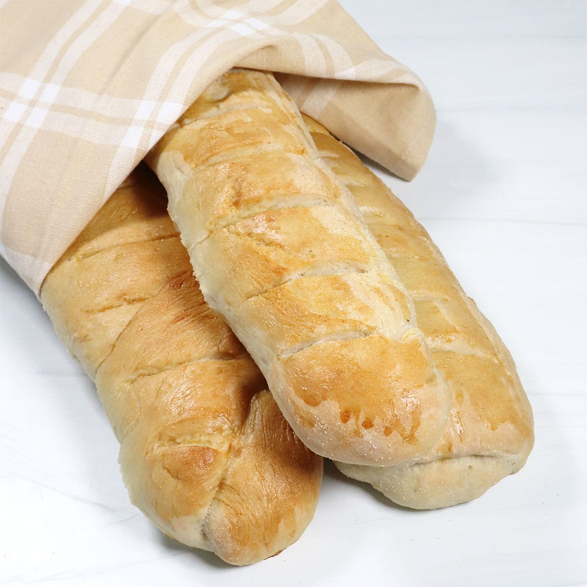 Three homemade French Bread loaves wrapped in towel.