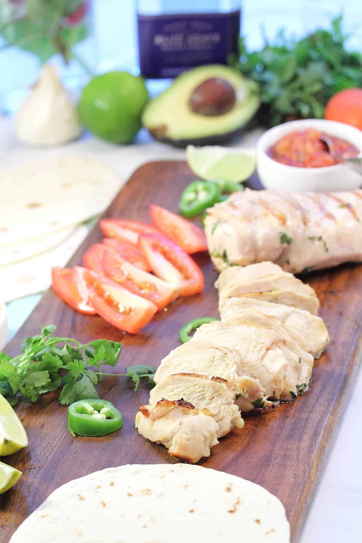 Sliced and whole grilled tequila chicken on wooden board with sliced tomatoes jalapeno and salsa.