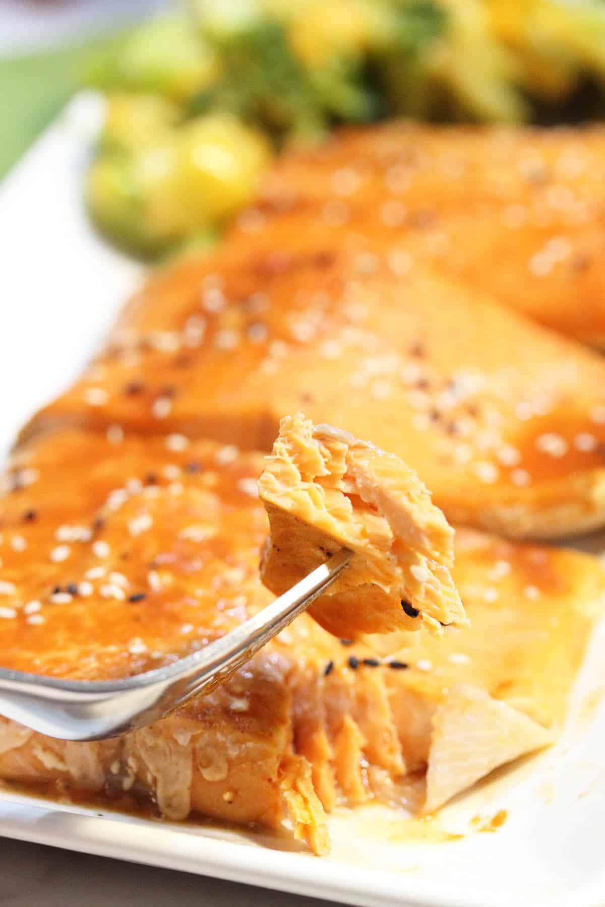 Bite of salmon on fork over white platter.