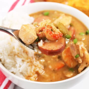 Spoonful of gumbo with shrimp and sausage over bowl.