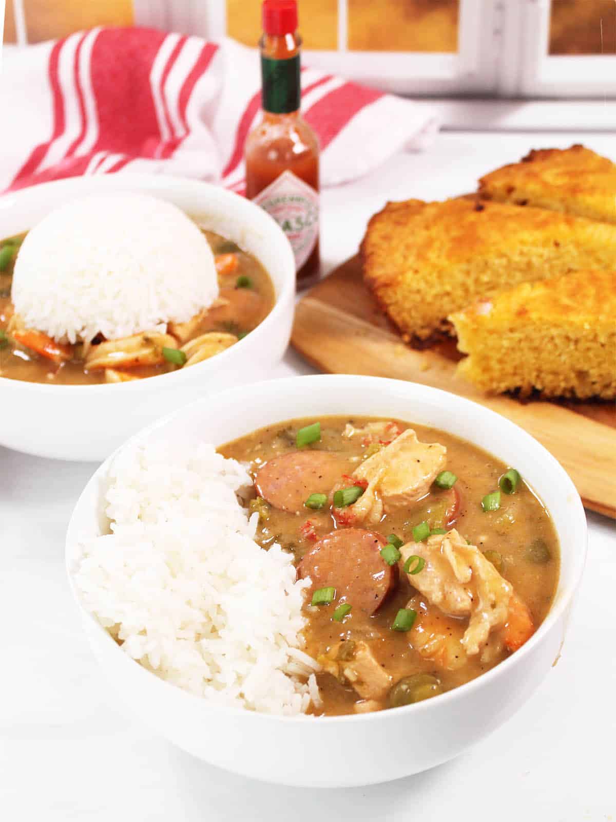 Two bowls of shrimp and sausage gumbo with rice and hot sauce.