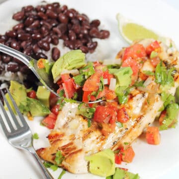 Spooning avocado salsa over grilled chicken.