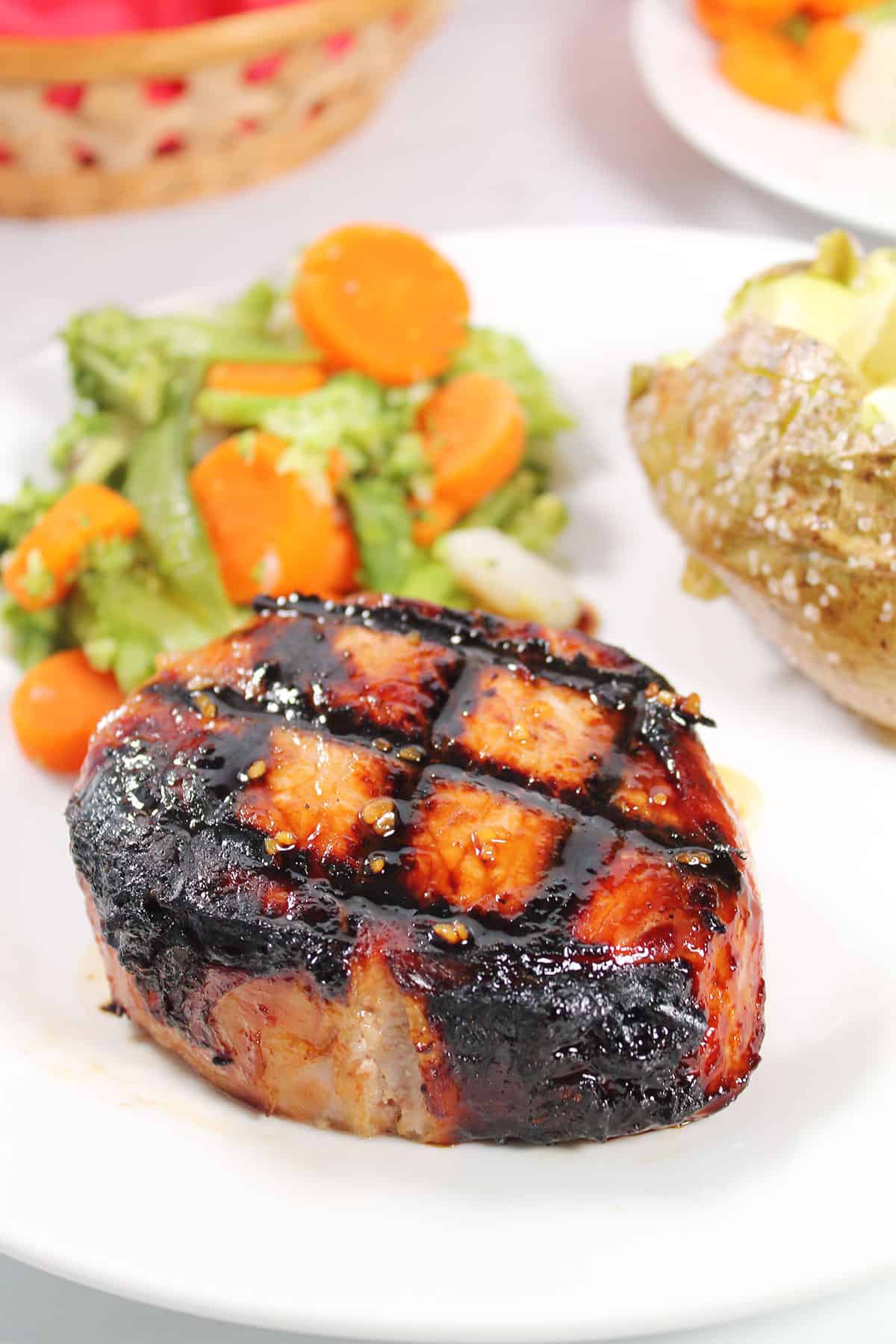Grilled honey garlic pork chop on plate with side dishes.