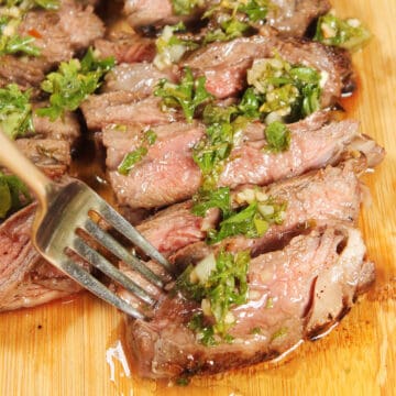 Fork in sliced skirt steak with chimichurri.