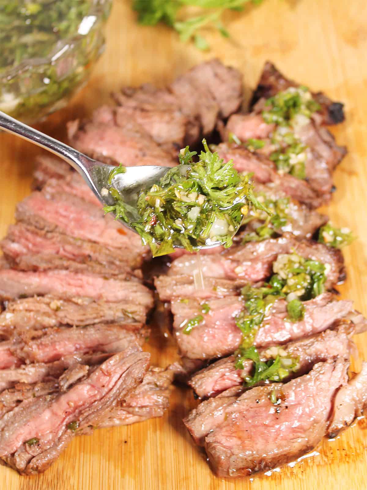 Spooning chimichurri steak marinade on steak.
