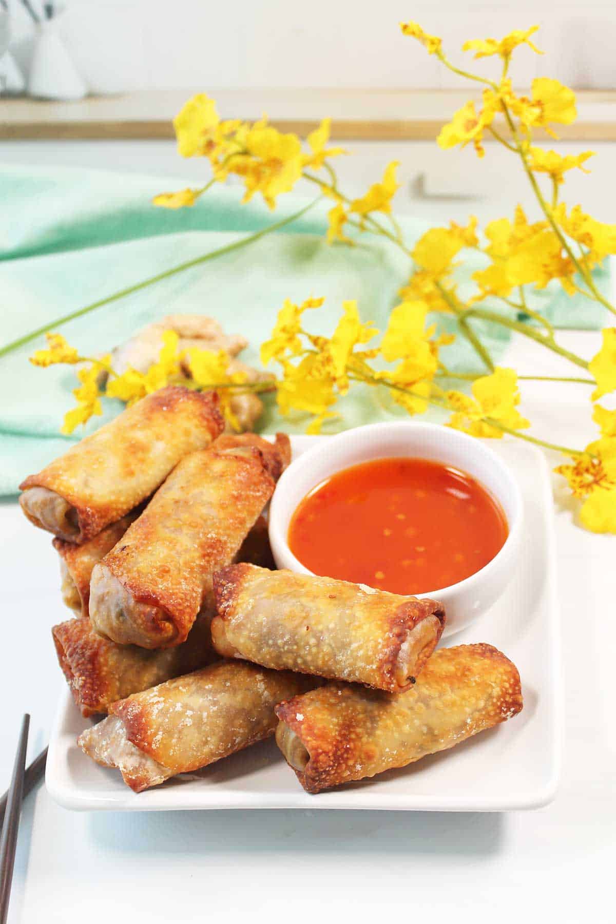Stacked air fryer vegetable egg rolls on a plate with sweet chili sauce for dipping.