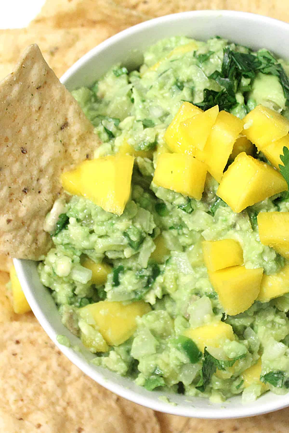 Closeup Mango Pineapple Guacamole in white bowl with chip in it.