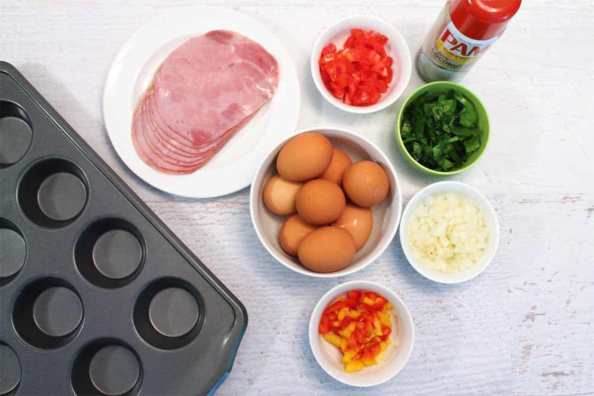 Ingredients for baked egg cups with muffin pan on white table.