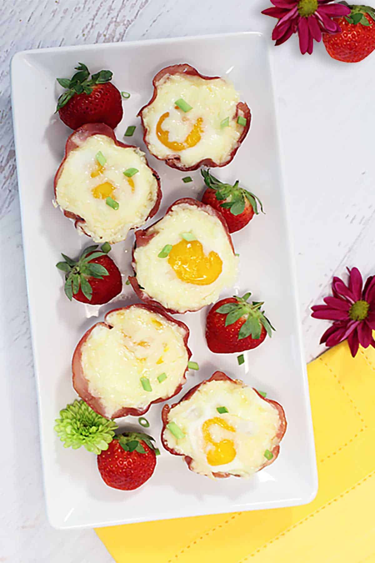 Overhead of ham cheese and egg cups on white platter with yellow napkin.