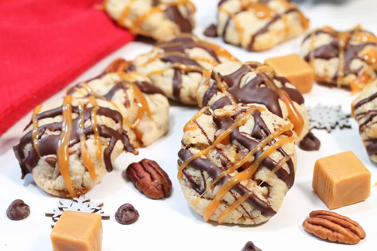 Turtle cookies laying on white table with caramels and pecans.