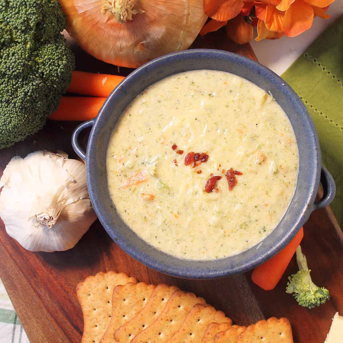 Overhead of single bowl of cheddar and broccoli soup on wooden board with vegetables.