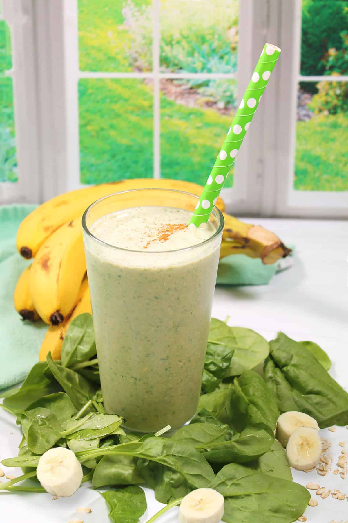 Spinach Banana Smoothie in glass with straw among spinach leaves.