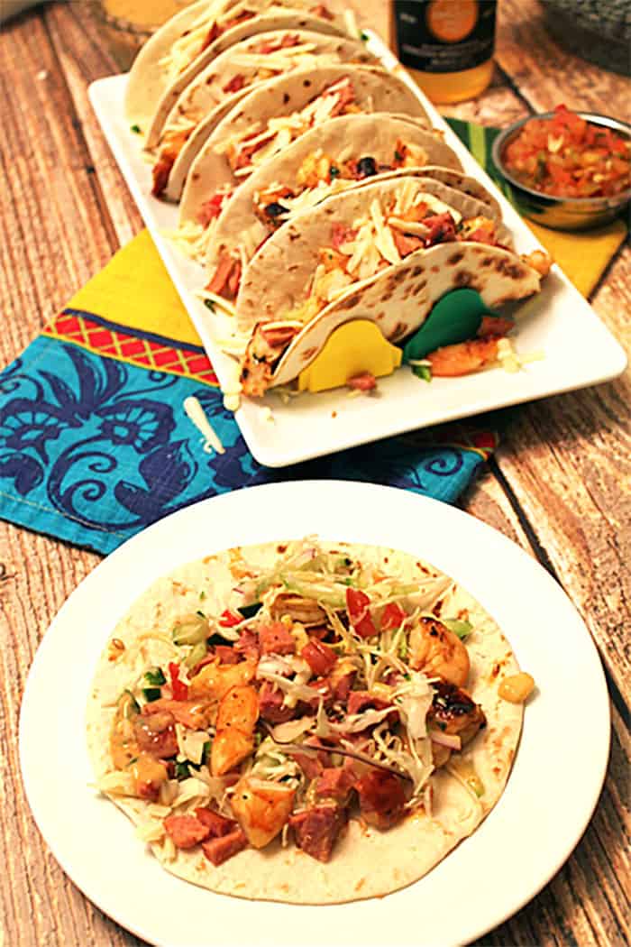 Open faced filled taco on white plate with filled tacos in background.