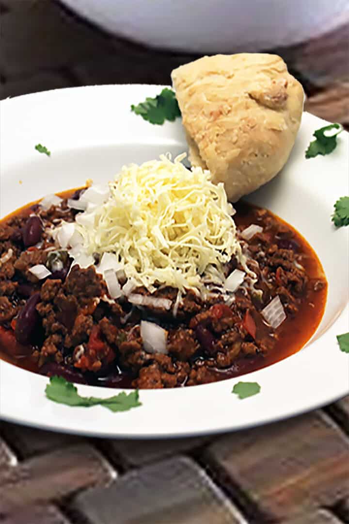 Chili in white bowl with parsley garnish and slice of bread.