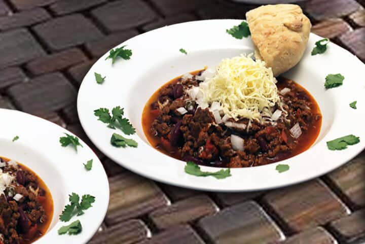 Serving of hearty beef chili in white bowl on brick surface.