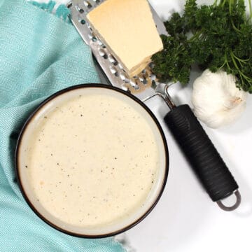 Overhead of white wine sauce with asiago cheese in bowl with green napkin.