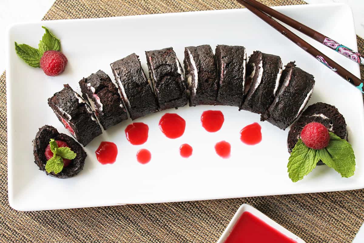 Closeup overhead of fruit sushi on white platter with raspberry sauce dots.