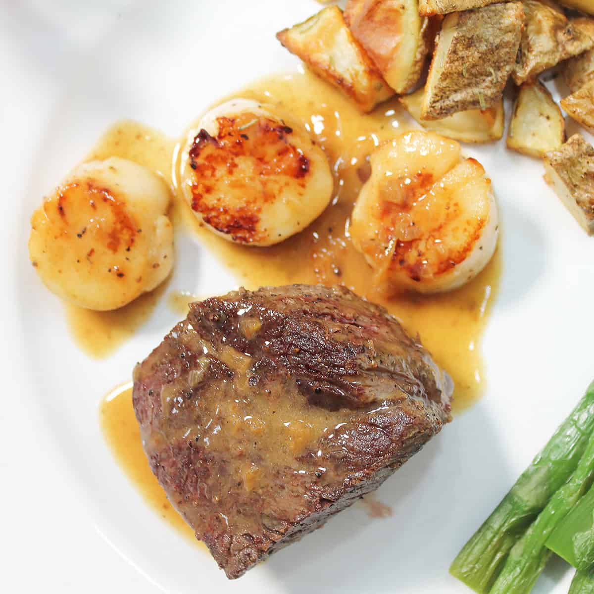 Overhead closeup of champagne butter sauce covered filet mignon and sea scallops.