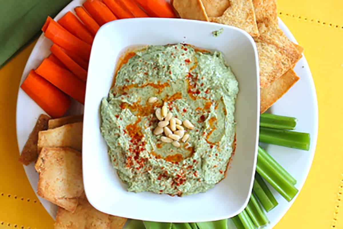 Closer overhead of hummus in white bowl with dippers.