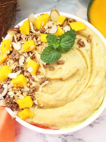 Closeup of smoothie in white flowered bowl with garnishes of coconut mango and granola.