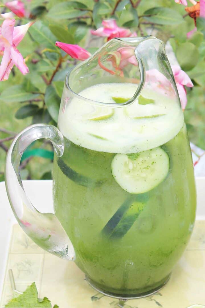 Pitcher of cucumber vodka drink with flowers in back.