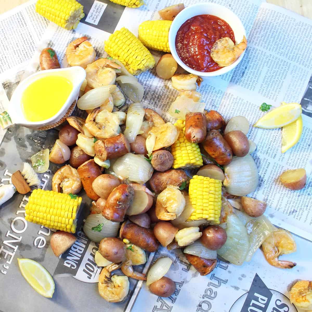 Overhead of shrimp boil on newspaper with butter and cocktail sauce.