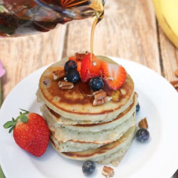 Pouring syrup over pancakes with fruit on top.