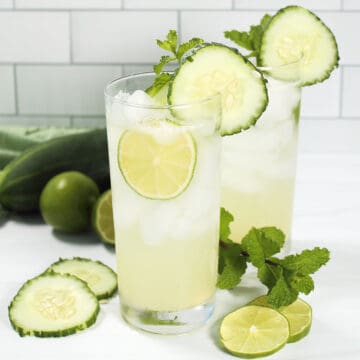 Closeup of two cocktails with cucumber and mint garnish.