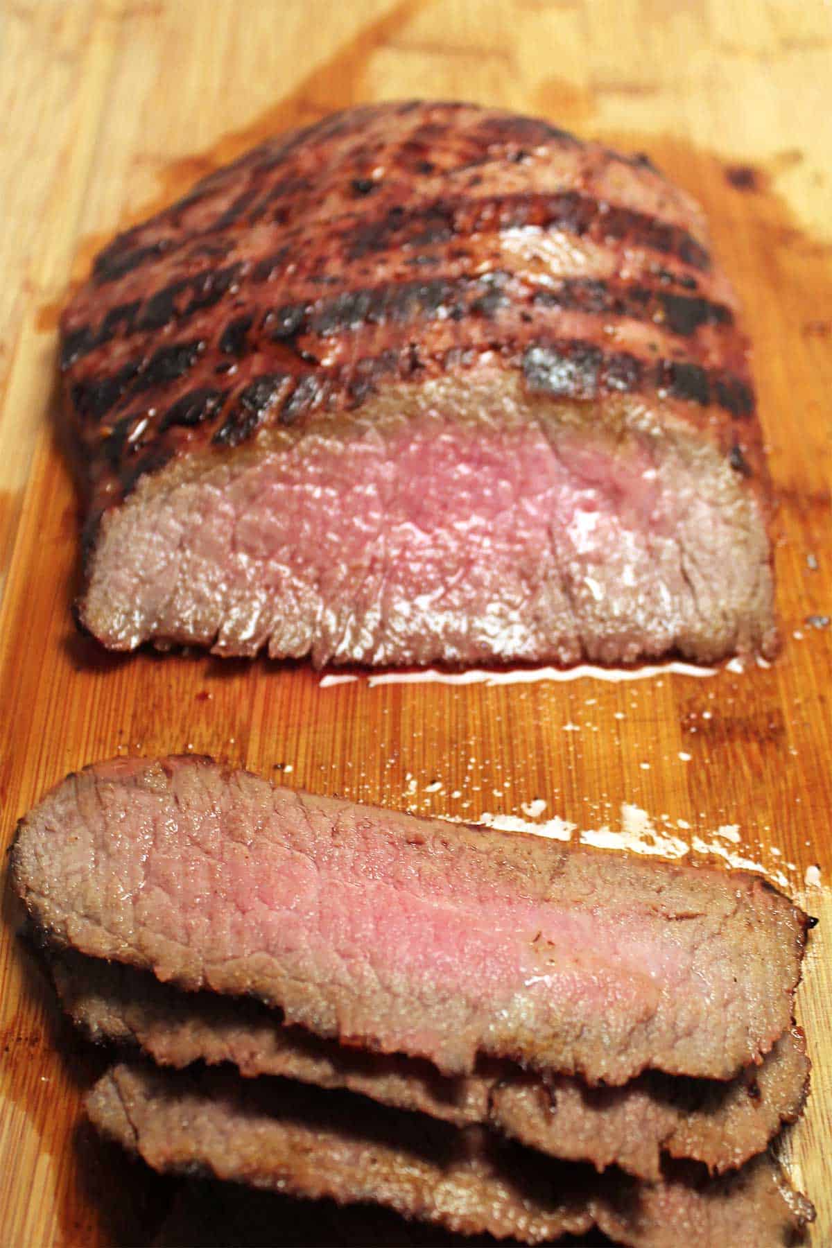 Partially sliced flank steak on cutting board.