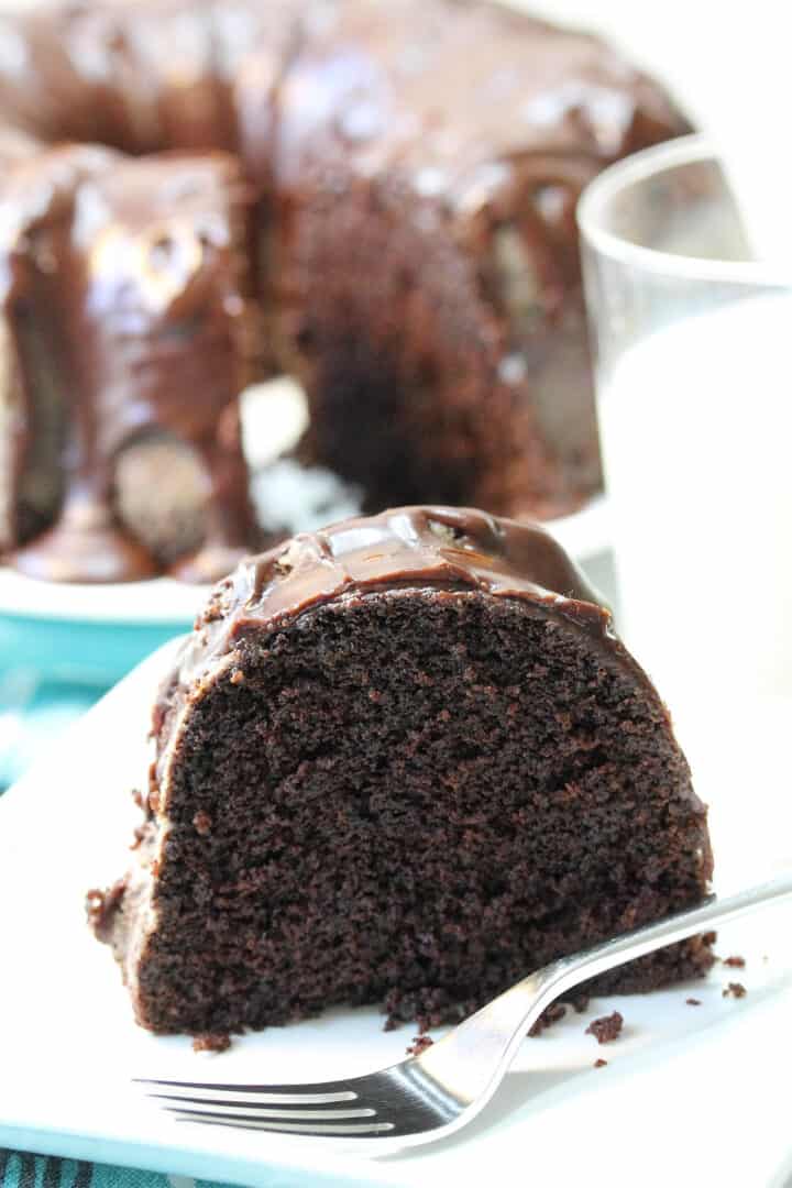 Slice of cake on white plate with fork and cake in background.