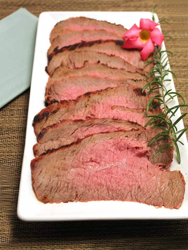 Sliced london broil on white platter with orchid.