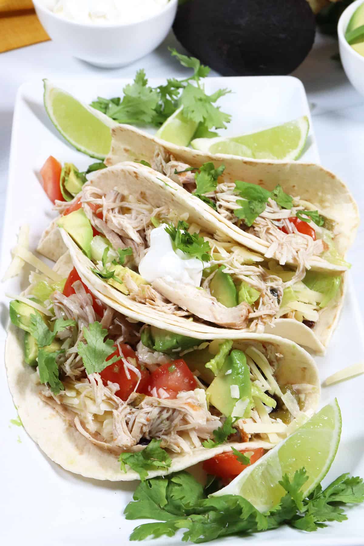3 Slow Cooker Chicken Tacos on platter with garnishes.