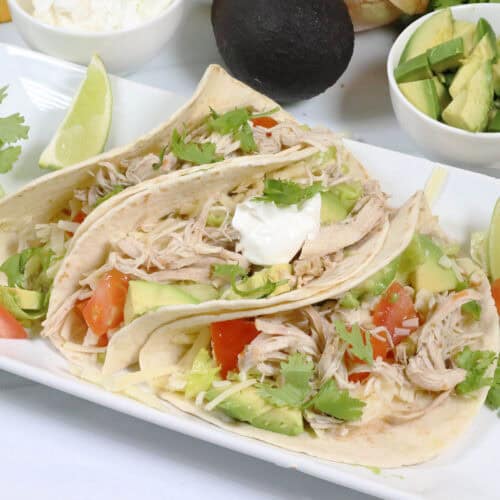3 slow cooker chicken tacos on platter with garnishes in back.