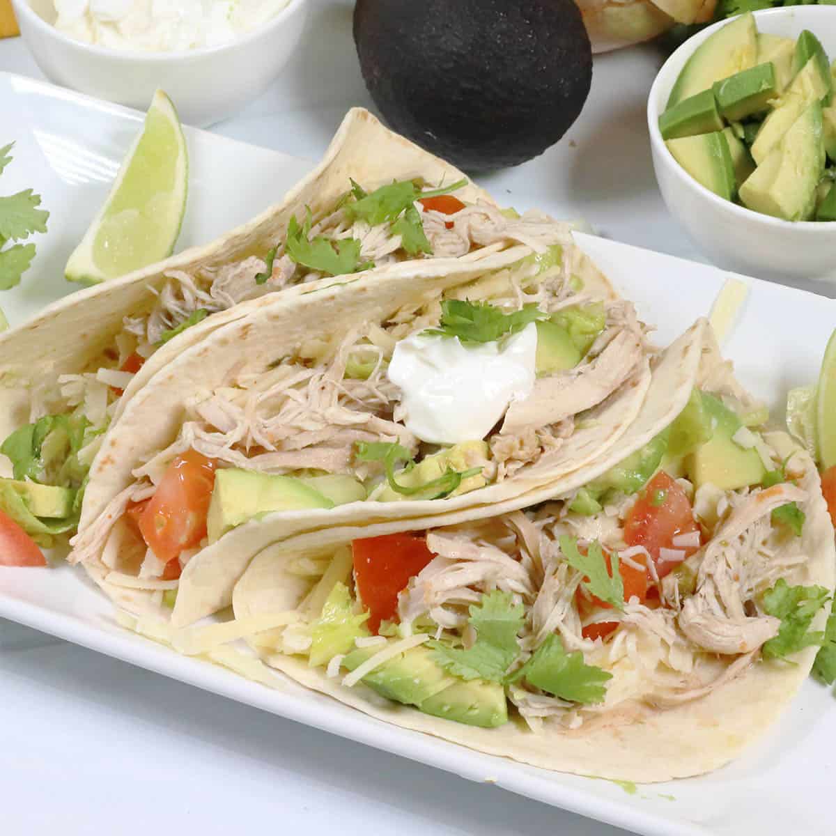 3 slow cooker chicken tacos on platter with garnishes in back.