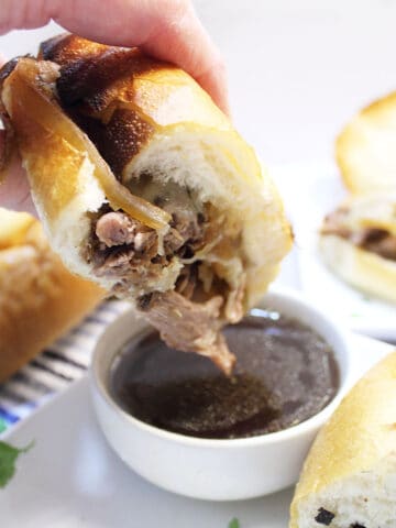 Dipping french dip sandwich into au jus.