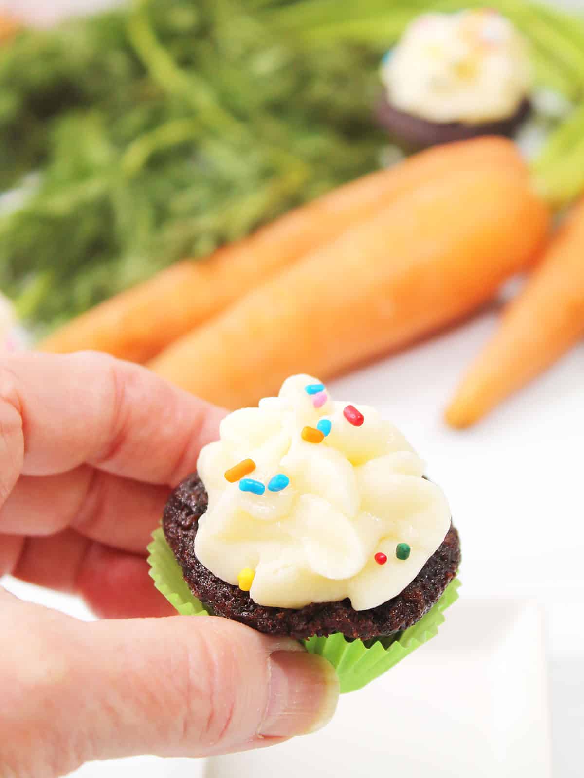 Holding a mini cupcake with cream cheese frosting.