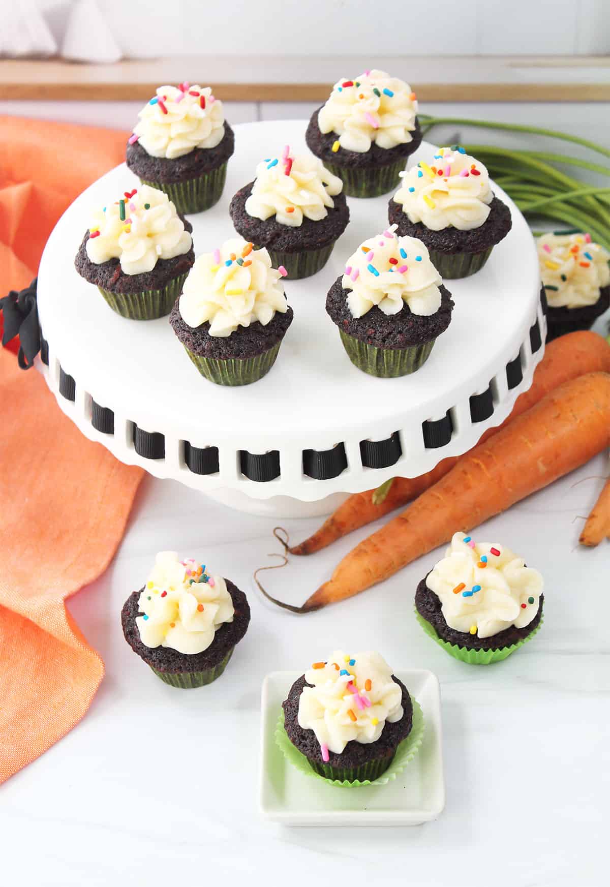 Finished carrot cake cupcakes with frosting and sprinkles on cake stand.
