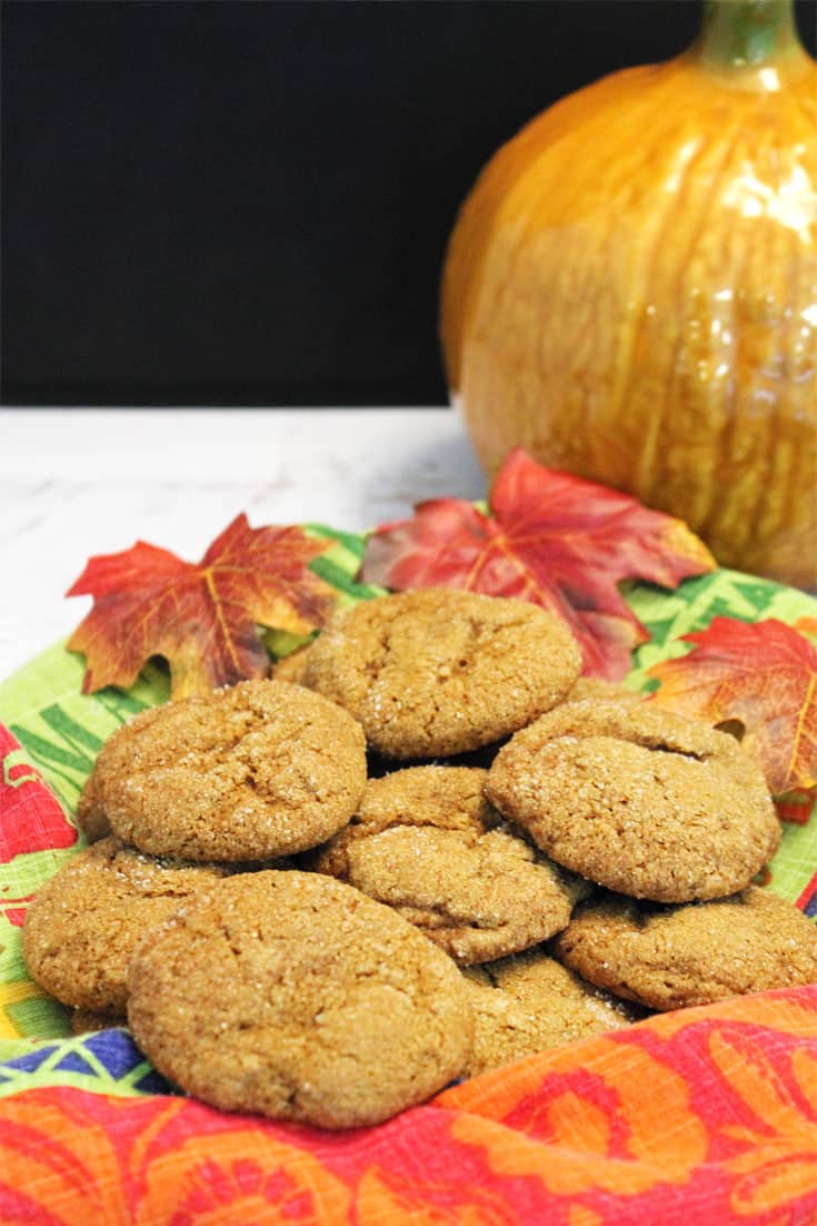 A basket of cookies lined with fall towel on white table with pumpkin in background.