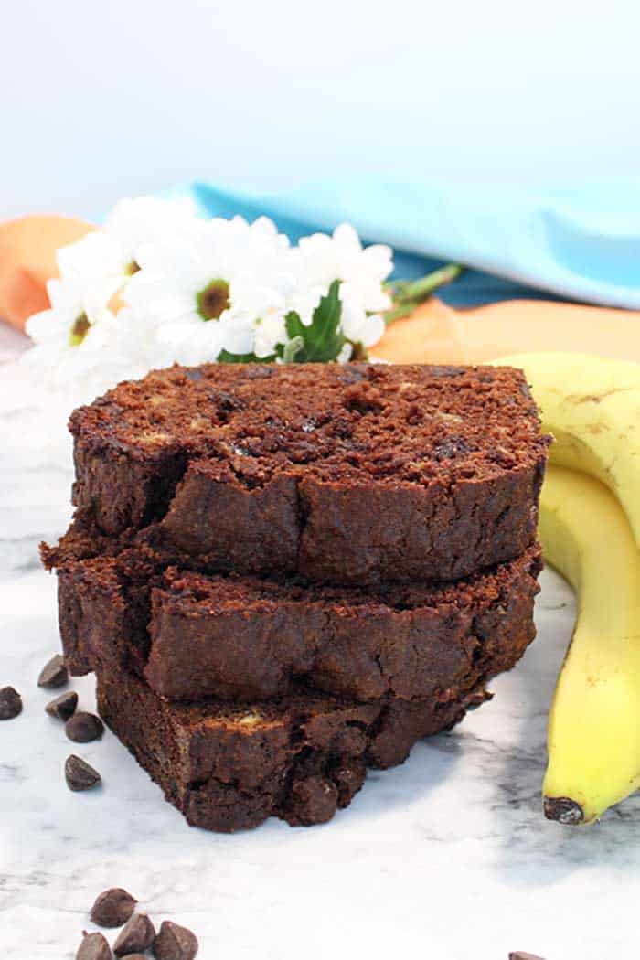 Stacked slices of chocolate banana bread next to bananas and daisies.