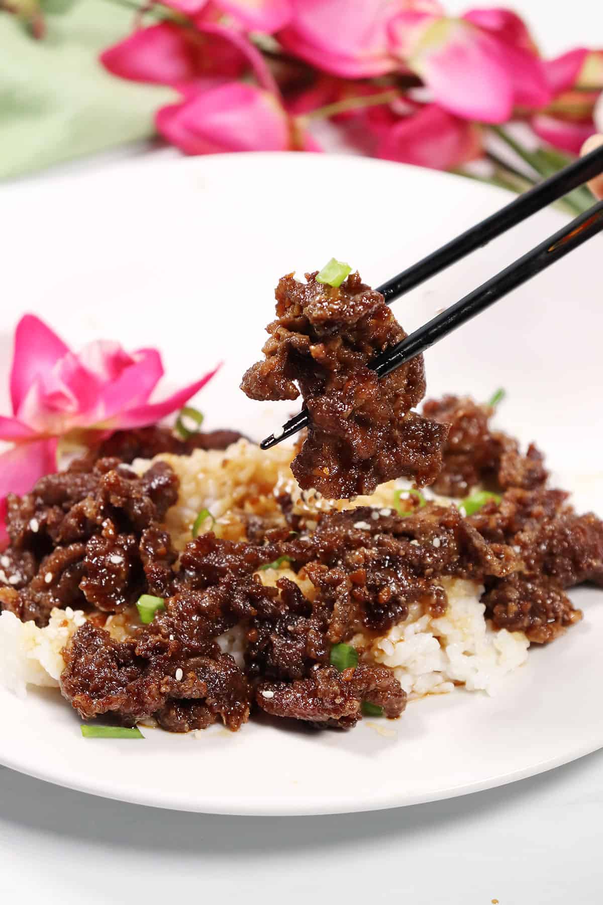 Holding slice of Mongolian Beef on chopsticks over plated dinner.