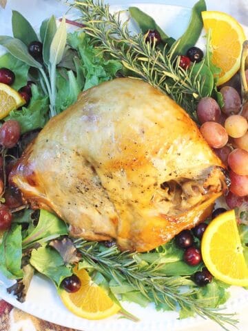 Overhead of turkey on white platter decorated with herbs and fruit.